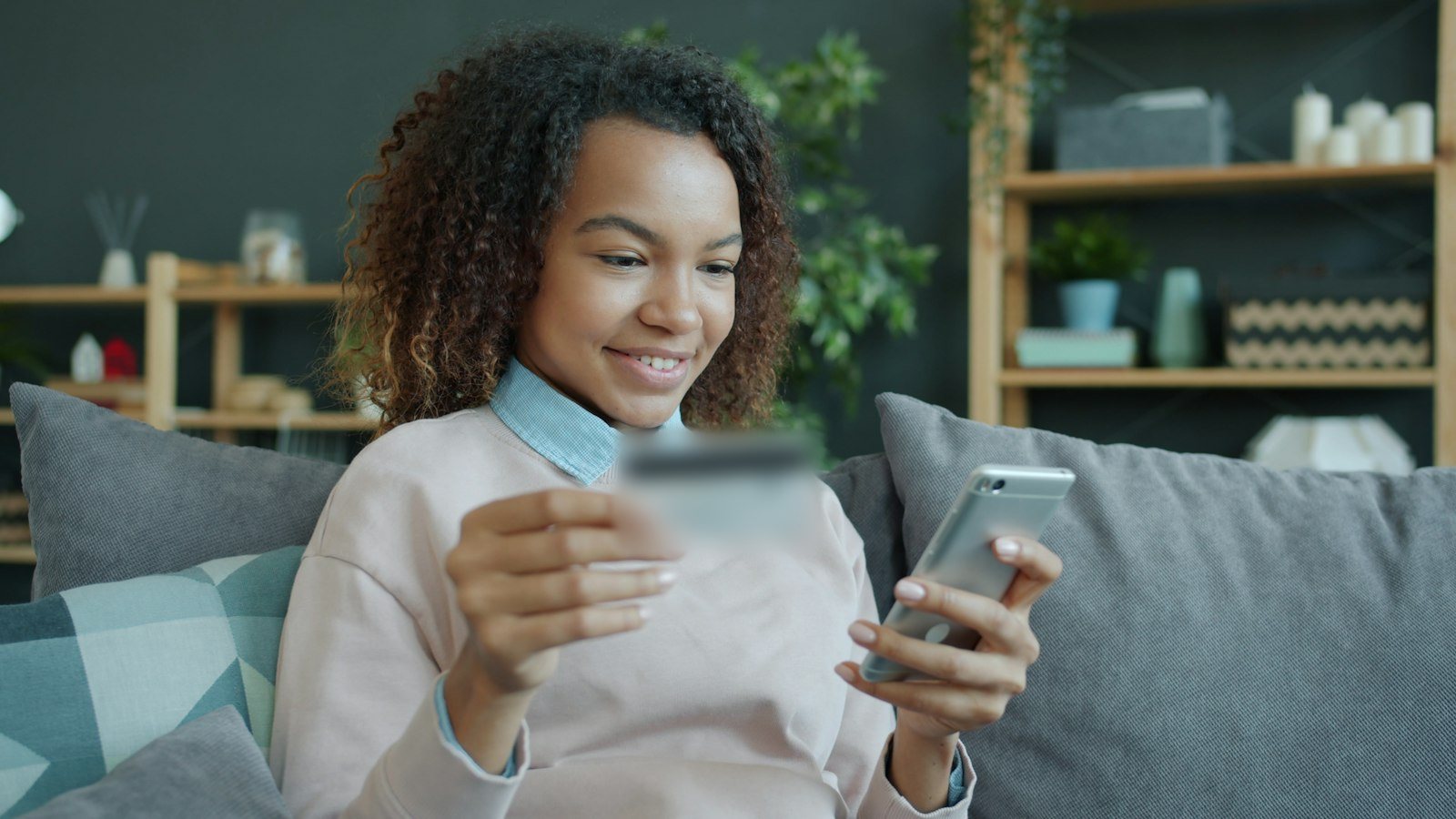 A smiling young woman on a sofa paying for an online order on her phone